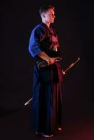 Kendo Kämpfer tragen im ein Rüstung, traditionell Kimono ist halten seine Helm und shinai Bambus Schwert während posieren auf ein schwarz Hintergrund. schließen hoch. foto