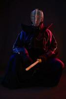 schließen hoch. Kendo Kämpfer tragen im ein Rüstung, traditionell Kimono, Helm, Sitzung, üben kriegerisch Kunst mit shinai Bambus Schwert, schwarz Hintergrund. foto