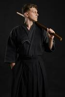 Kendo Guru tragen im ein traditionell japanisch Kimono ist üben kriegerisch Kunst mit das shinai Bambus Schwert gegen ein schwarz Studio Hintergrund. foto