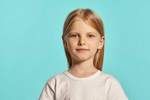 Nahansicht Studio Schuss von ein schön blond wenig Mädchen im ein Weiß T-Shirt posieren gegen ein Blau Hintergrund. foto