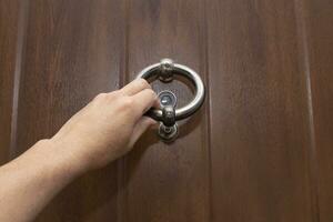 ein Hand halten ein Tür Klopfer. Klopfen auf ein hölzern Tür mit ein Metall Ring geformt Tür Klopfer. foto