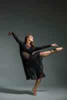 Tanzen Frau im ein schwarz Kleid. zeitgenössisch modern tanzen auf ein grau Hintergrund. foto