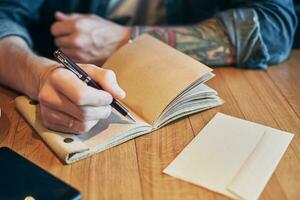 Mann Hand mit Stift Schreiben auf Notizbuch auf ein hölzern Tisch. Nahansicht foto