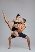 das Paar von ein jung modern Ballett Tänzer im schwarz Anzüge sind posieren Über ein grau Studio Hintergrund. foto