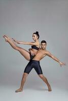 das Paar von ein jung modern Ballett Tänzer im schwarz Anzüge sind posieren Über ein grau Studio Hintergrund. foto