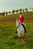 jung Frau Fahrer, tragen rot redingote und Weiß Hose, mit ihr Pferd im Abend Sonnenuntergang Licht. foto