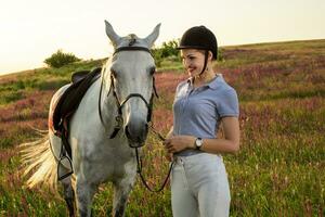 Jockey jung Mädchen Petting und umarmen Weiß Pferd im Abend Sonnenuntergang foto