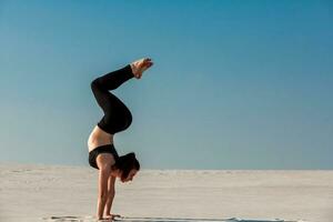 jung Frau üben Handstand auf Strand mit Weiß Sand und hell Blau Himmel foto