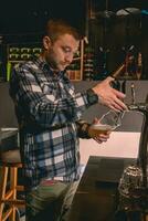 bärtig Barmann Füllung Glas mit ungefiltert Bier von Zapfhahn im Kneipe foto