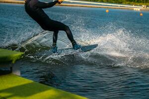 Wakeboarder Schneiden Wasser mit Kante von Tafel Erstellen spritzt während beginnend aus Dock foto