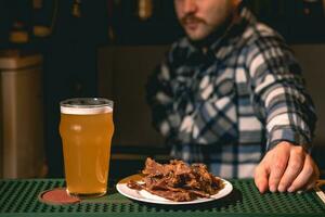 Glas von Weizen Bier und Teller mit getrocknet Fleisch Streifen auf Bar Zähler foto