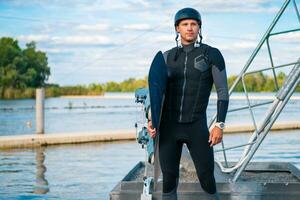 zuversichtlich Wakeboarder Stehen auf Seebrücke mit Tafel im Hand foto