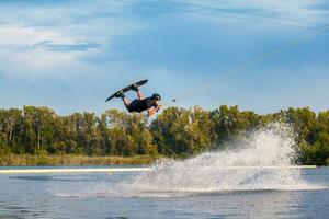 zuversichtlich Mann meisterhaft Springen Über Wasser Oberfläche von Fluss auf Wakeboard foto