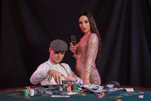 Mann spielen Poker beim Kasino Sitzung beim Tabelle mit Stapel von Chips, Geld, Sekt, Karten. feiern Sieg mit Frau. schwarz Hintergrund. Nahansicht. foto