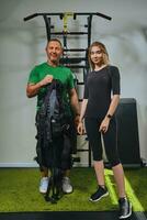 muskulös Fitness Lehrer ist Putten auf ein ems passen zum sportlich Frau. Ausbildung im ein Fitnessstudio durch ein Methode zu erhöhen, ansteigen Energie. foto