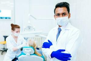 Porträt von ein jung zuversichtlich asiatisch männlich Zahnarzt im Klinik im Vorderseite von wweiblich Zahnarzt Überprüfung Zähne zu geduldig. Dental Klinik Konzept foto