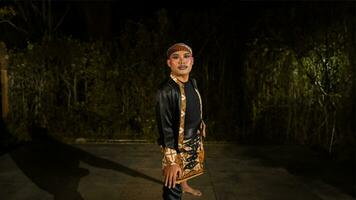 ein indonesisch Mann Tänze mit Entschlossenheit und Fertigkeit während tragen ein schwarz Kostüm auf Bühne foto