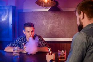 zwei jung Männer Rauch elektronisch Zigaretten im ein vapebar foto