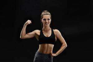 Schuss von ein stark Frau mit muskulös Abdomen im Sportbekleidung. Fitness weiblich Modell- posieren auf schwarz Hintergrund. foto
