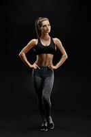 Schuss von ein stark Frau mit muskulös Abdomen im Sportbekleidung. Fitness weiblich Modell- posieren auf schwarz Hintergrund. foto