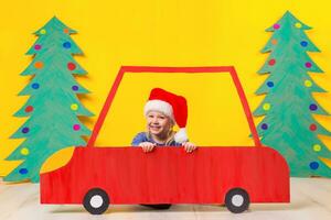 Kind mit Weihnachten Hut Fahren ein Auto gemacht von Karton. Weihnachten Konzept. Neu Jahre Feiertage. foto