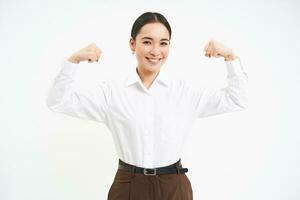 Geschäft und korporativ Frauen. stark und erfolgreich asiatisch Frau Unternehmer, zeigt an Bizeps, Biegen Muskeln, lächelnd erfreut, Weiß Hintergrund foto