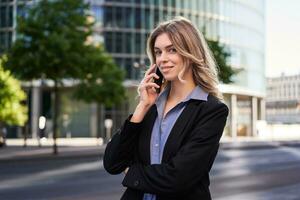 Porträt von erfolgreich Geschäftsfrau, Unternehmen Vorsitzender Spaziergänge auf Straße und macht Telefon Anrufe, reden auf Smartphone foto