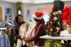 selektiv Fokus von Frauen im Kleidung speichern, suchen beim Kleider auf Kleiderbügel während Weihnachten Jahreszeit Der Umsatz beim Einkaufszentrum. Klient und Mitarbeiter Mitglied Analysieren Stoff zu Hilfe wählen perfekt Weihnachten gegenwärtig. foto