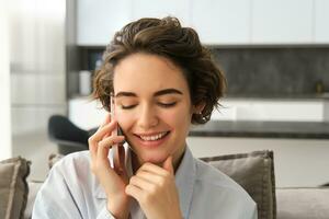 schließen oben Porträt von lächelnd schön Frau, reden auf Handy, Mobiltelefon Telefon, Chats auf Smartphone, Anrufe jemand, sitzt beim Zuhause foto