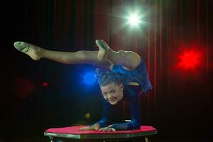 ein Mädchen mit ein flexibel Körper. führt aus ein Zirkus Künstler. Zirkus Turner. balancieren Gesetz. das Kind führt aus ein akrobatisch Trick foto