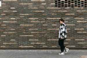 jung Mann Spaziergänge Nieder das Straße im Vorderseite von ein Backstein Mauer foto