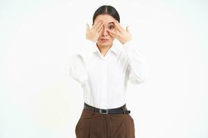 Porträt von jung asiatisch Frau Abdeckungen ihr Augen mit Hände, versteckt sich von etwas, Weiß Hintergrund foto