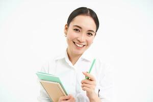 schön zuversichtlich Koreanisch Frau, Schüler mit Stift und Notizbücher, lächelnd und suchen Glücklich, Stehen Über Weiß Hintergrund foto