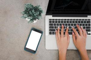 Draufsicht einer Frauenhand, die eine Laptop-Computertastatur und ein Mobiltelefon verwendet, verspotten einen leeren Bildschirm. foto