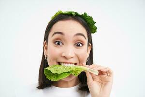 Glücklich, süß asiatisch Frau Essen Grün Kopfsalat, Vegetarier Likes oranisch Gemüse, Weiß Studio Hintergrund foto