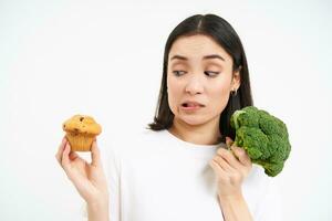 Bild von Vegetarier Mädchen, vermeidet Gebäck, Stöcke zu Brokkoli, Essen Gemüse stattdessen von Cupcake, Weiß Hintergrund foto