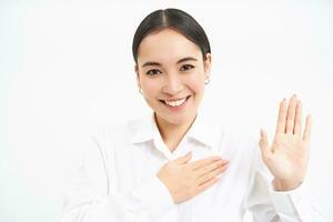 freundlich jung Geschäftsfrau, asiatisch Dame erhöht einer Hand und setzt Palme auf Herz, macht verspricht, stellt vor Sie selber, steht Über Weiß Hintergrund foto