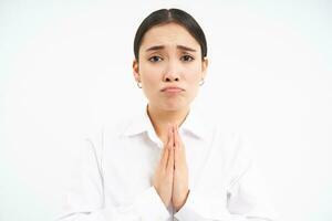 verärgert jung Verkäuferin, asiatisch Frau hält Hände im beten, bittet Du, fragt zum Gefallen mit traurig Gesicht, Bitten, Stehen Über Weiß Hintergrund foto