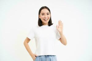 freundlich lächelnd Koreanisch Frau, Wellen Hand sagt Hallo, Hallo Geste, Gruß Du, Stehen Über Weiß Hintergrund foto