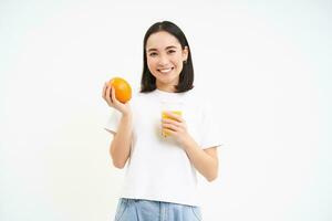 lächelnd jung und gesund Frau, hält Orange und Glas von Saft, macht frisch trinken, steht Über Weiß Hintergrund foto