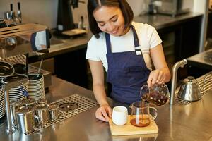 Barista im Cafe Gießen Filter Kaffee, brauen und vorbereiten bestellen hinter Schalter, tragen Blau Schürze foto