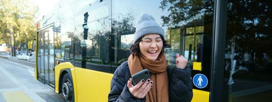 modern Menschen und Lebensstil. glücklich asiatisch Mädchen Geschrei von Freude, feiert, steht in der Nähe von Bus Öffentlichkeit Transport und sieht aus erstaunt foto