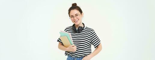 jung Frau mit Notizbücher, Bücher und Studie Material, posieren Über Weiß Hintergrund, trägt Kopfhörer Über Hals foto