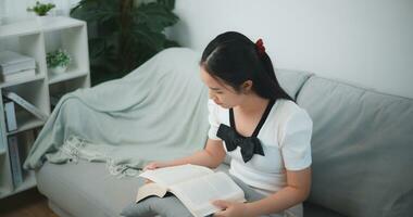 Porträt von jung asiatisch Frau Sitzung entspannend auf Couch und lesen Buch im Leben Zimmer, Ausgaben Freizeit Zeit beim heim. foto