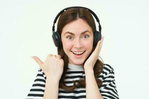 Porträt von aufgeregt Frau im kabellos Kopfhörer, zeigen genial Nachricht, zeigen links, Stehen Über Weiß Hintergrund foto