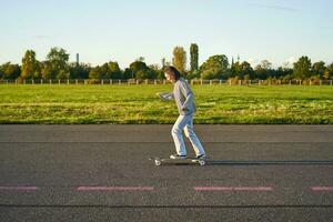 Hobbys und Lebensstil. jung Frau Reiten Skateboard. Skater Mädchen genießen Kreuzfahrt auf Longboard auf sonnig Tag draußen foto