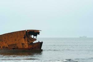 rostig Schiffswrack gegen ein nebelig Seelandschaft mit ein Schiff im das Entfernung foto