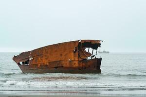 rostig Schiffswrack gegen ein nebelig Seelandschaft mit ein Schiff im das Entfernung foto