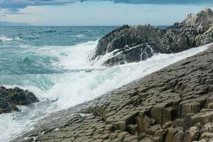 felsig Strand gebildet durch säulenförmig Basalt gegen das Surfen, Küsten Landschaft von das Kuril Inseln foto