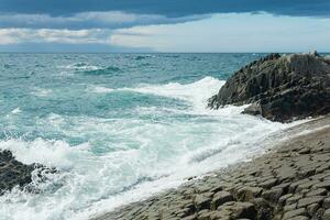 felsig Strand gebildet durch säulenförmig Basalt gegen das Surfen, Küsten Landschaft von das Kuril Inseln foto